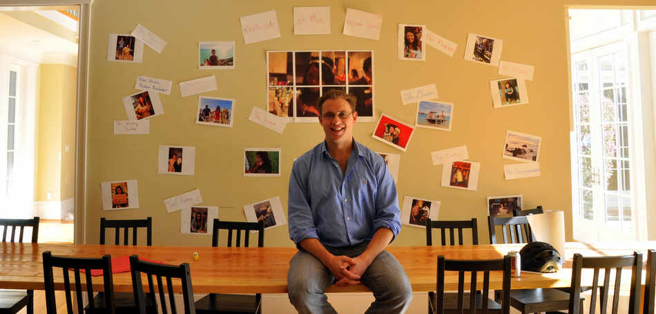 David Rohrsheim sitting at a table with photos on the wall behind him